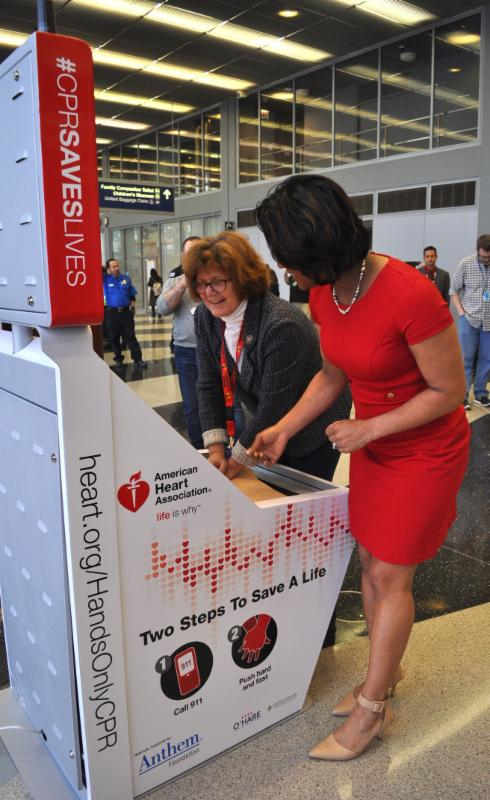 AHA Hands-Only CPR spokesperson Danielle DeVito, right, helps CDA Commissioner Ginger S. Evans learn how to use the CPR kiosk at O'Hare.