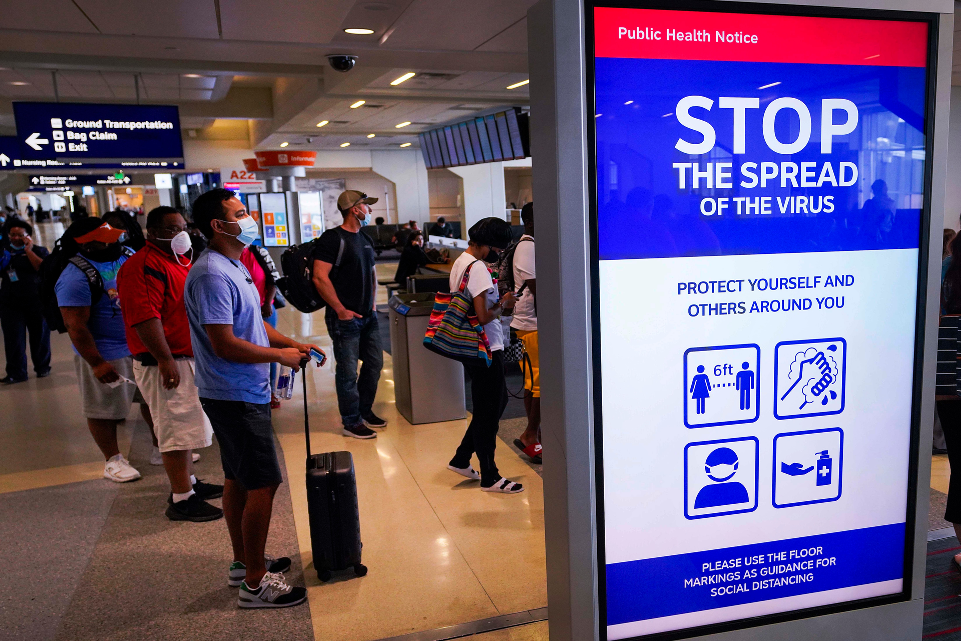 A message board displays a public health notice of precautions against the spread of COVID-19 as passengers wait to board an American Airlines flight at DFW International Airport Terminal A on Tuesday, June 30, 2020.