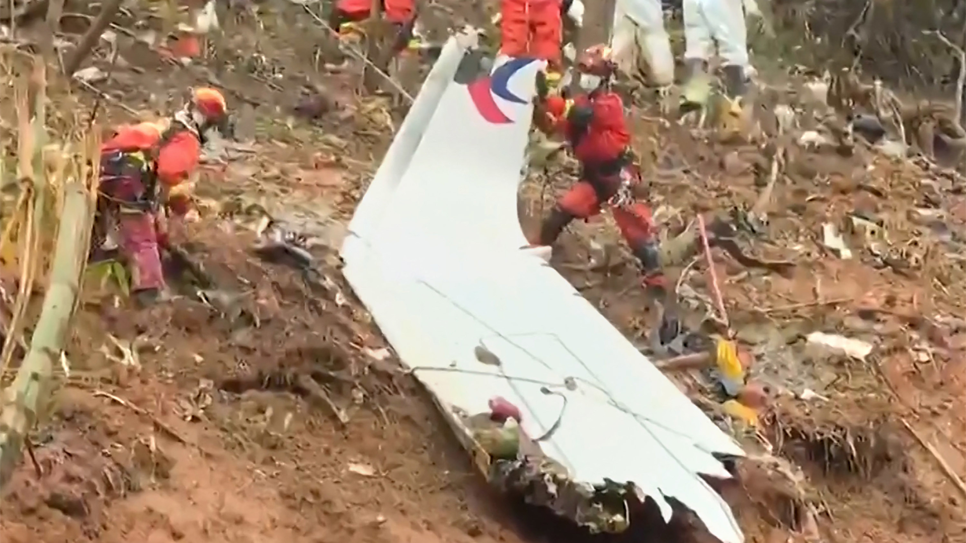 This screengrab taken on March 24, 2022, from video by state broadcaster China Central Television (CCTV) via AFPTV shows rescue teams with a piece of the fuselage as they continue their search at the site of where a China Eastern passenger jet crashed onto a mountainside near Wuzhou City in China's southern Guangxi region.