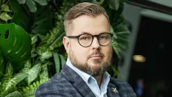 a man wearing glasses and a plaid suit looks into the camera, standing in front of greenery a man wearing glasses and a plaid suit looks into the camera, standing in front of greenery