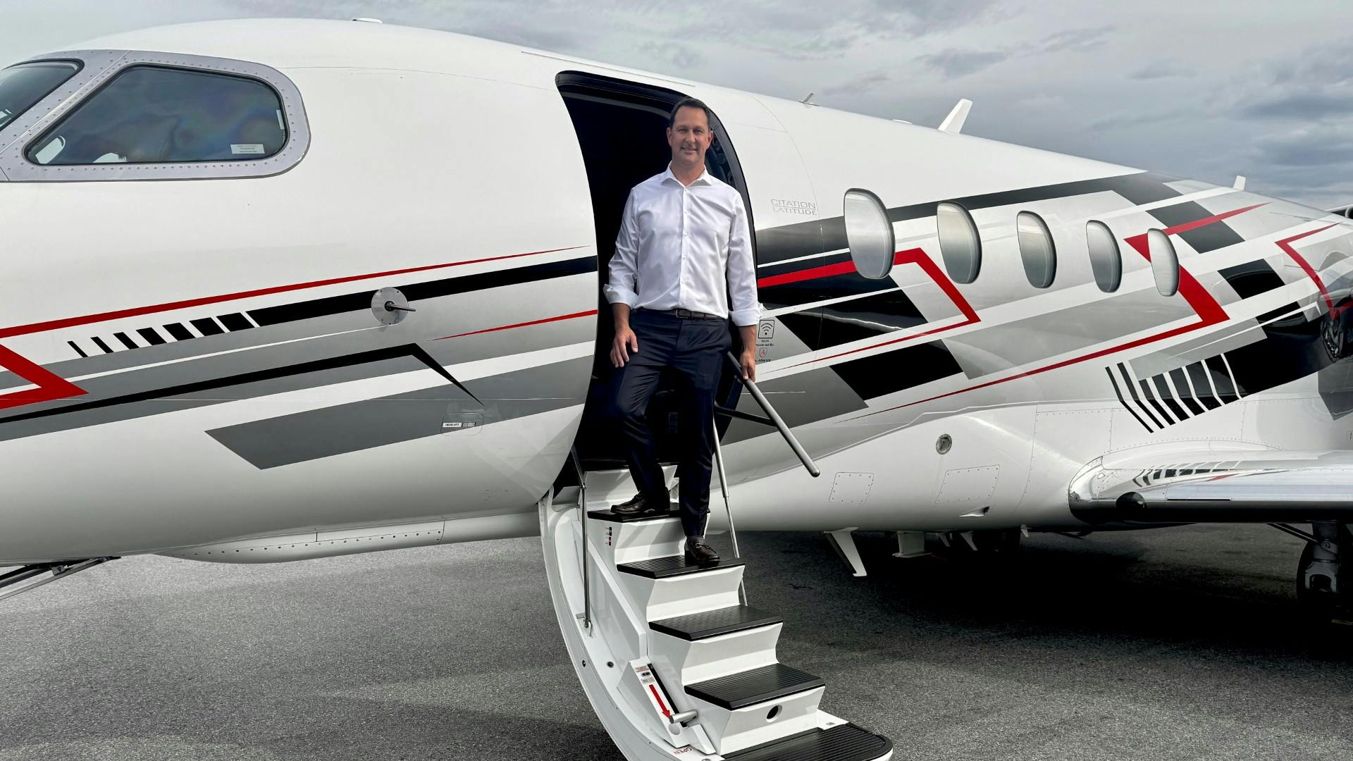 A man in business attire stepping out of a jet plane onto a staircase