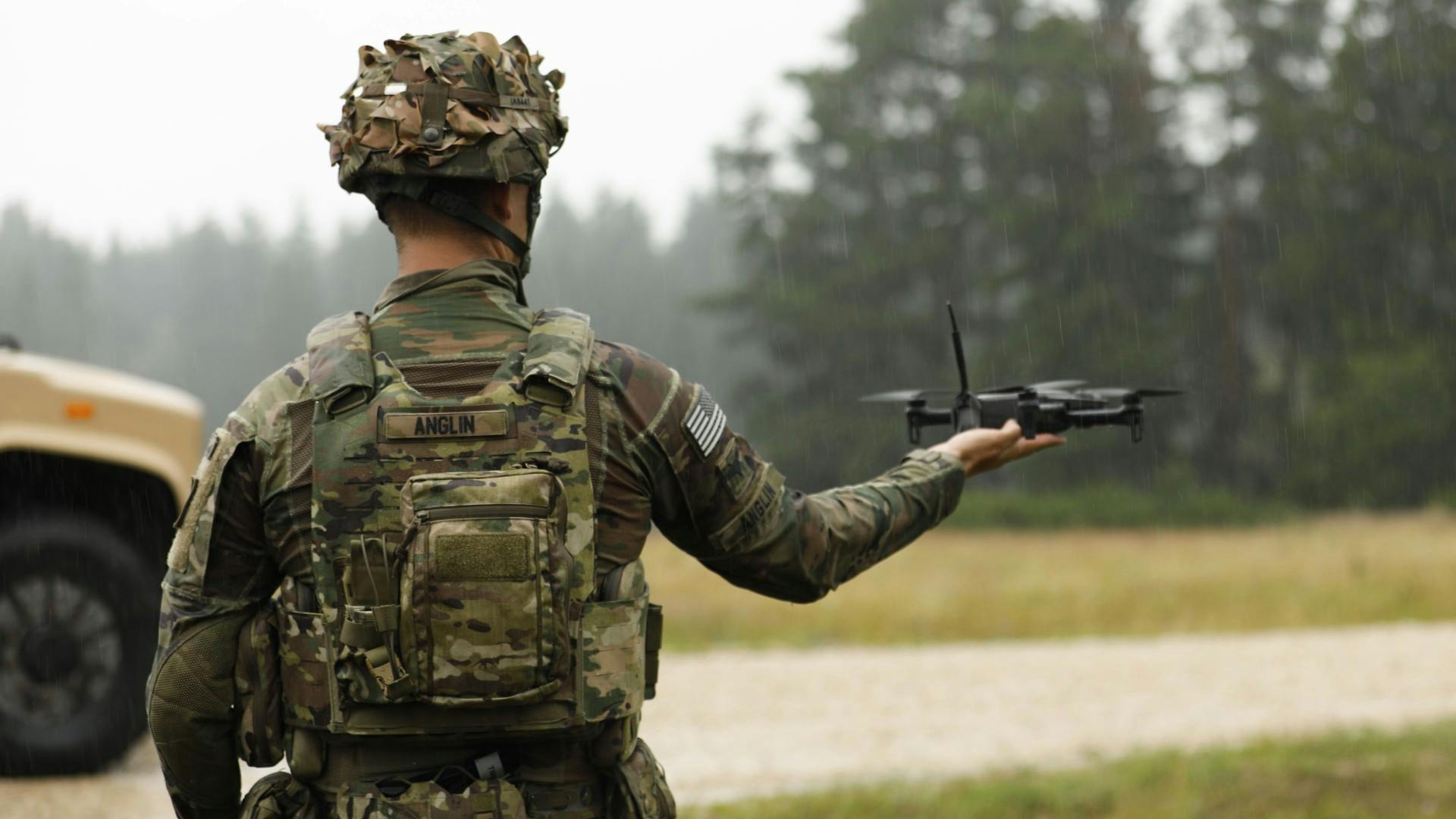 A person wearing military fatigues holds a drone in their hand