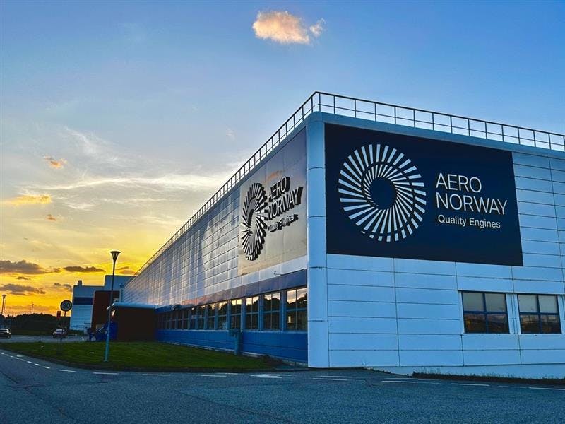 A large white building with a sign that reads 'Aero Norway Quality Engines' sits in front of a setting sun