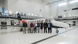 A group of professionals in business attire stand in front of an airplane in an airplane hangar, smiling at the camera A group of professionals in business attire stand in front of an airplane in an airplane hangar, smiling at the camera