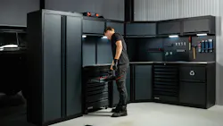 A man in black clothing standing next to a large system of black cabinets and shelves, with a tool box on the top of one of the shelves A man in black clothing standing next to a large system of black cabinets and shelves, with a tool box on the top of one of the shelves