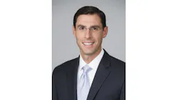 A man wearing a suit and tie and glasses smiles at the camera A man wearing a suit and tie and glasses smiles at the camera