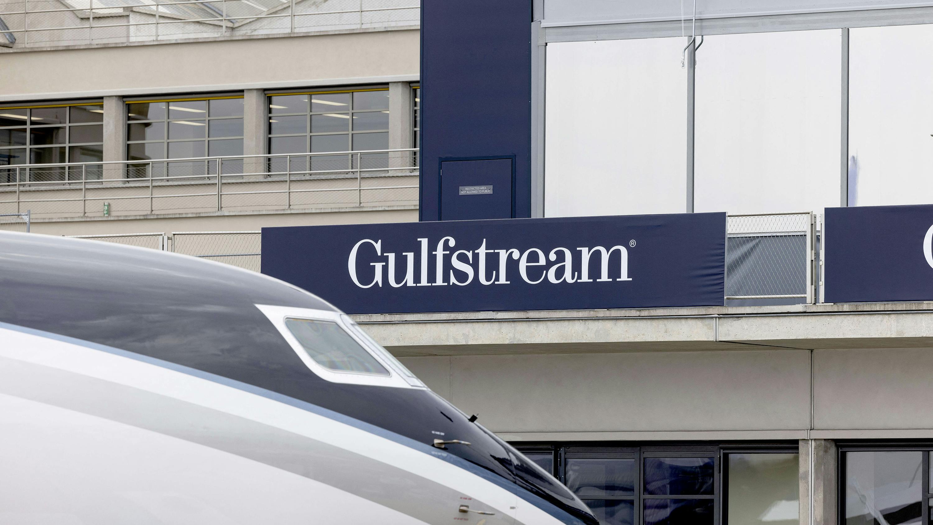 The front part of an airplane in front of a building with a sign on it that says, 'GULFSTREAM'