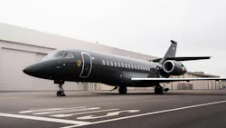 A large black airplane on a tarmac in front of beige buildings A large black airplane on a tarmac in front of beige buildings