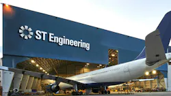 An airplane parked halfway into a maintenance hangar that has a sign on the front reading: ST Engineering An airplane parked halfway into a maintenance hangar that has a sign on the front reading: ST Engineering