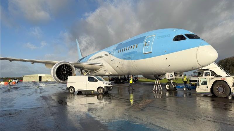 A white and blue airplane parked on a tarmac with a white van parked next to it on the ground
