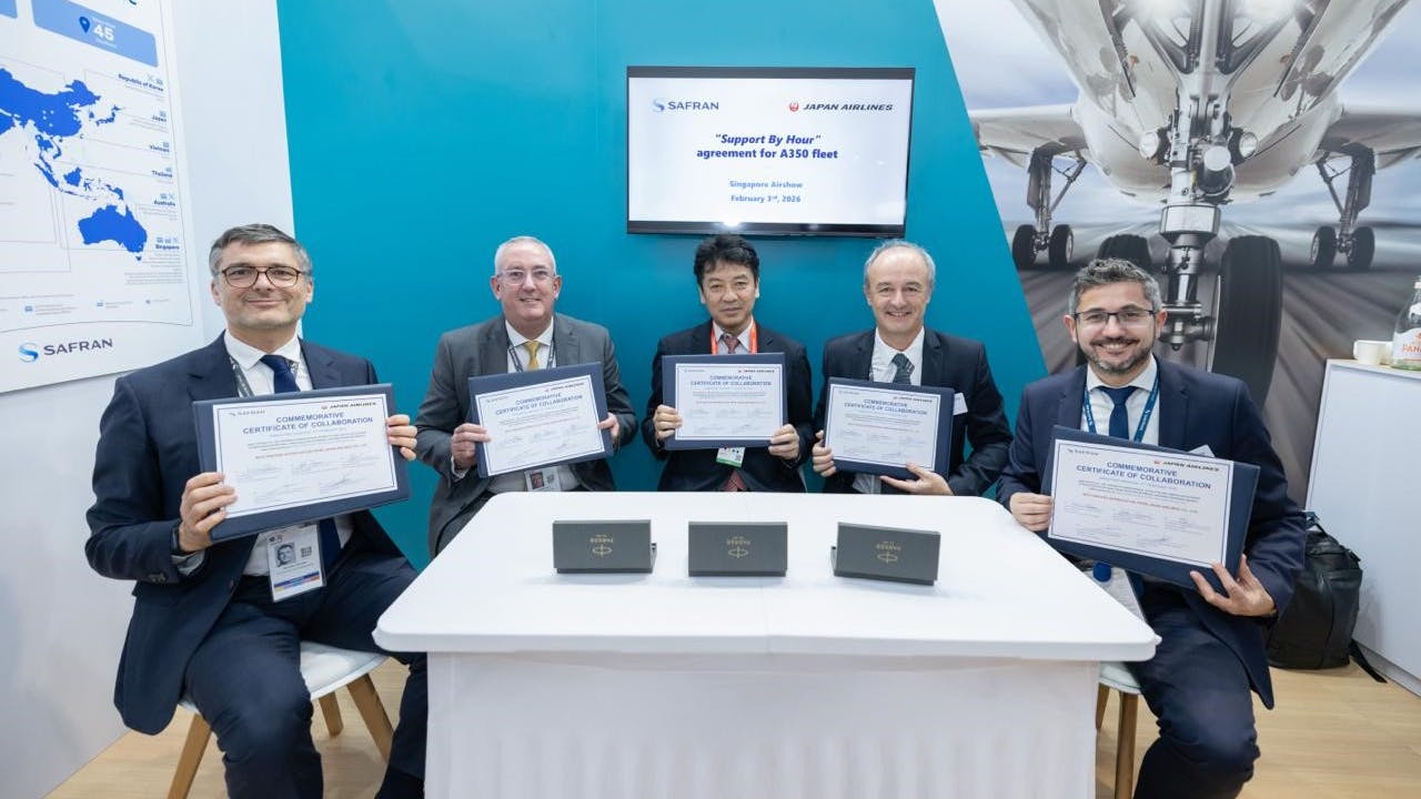 A group of men wearing suits sitting at a table and holding up framed certificates while smiling at the camera