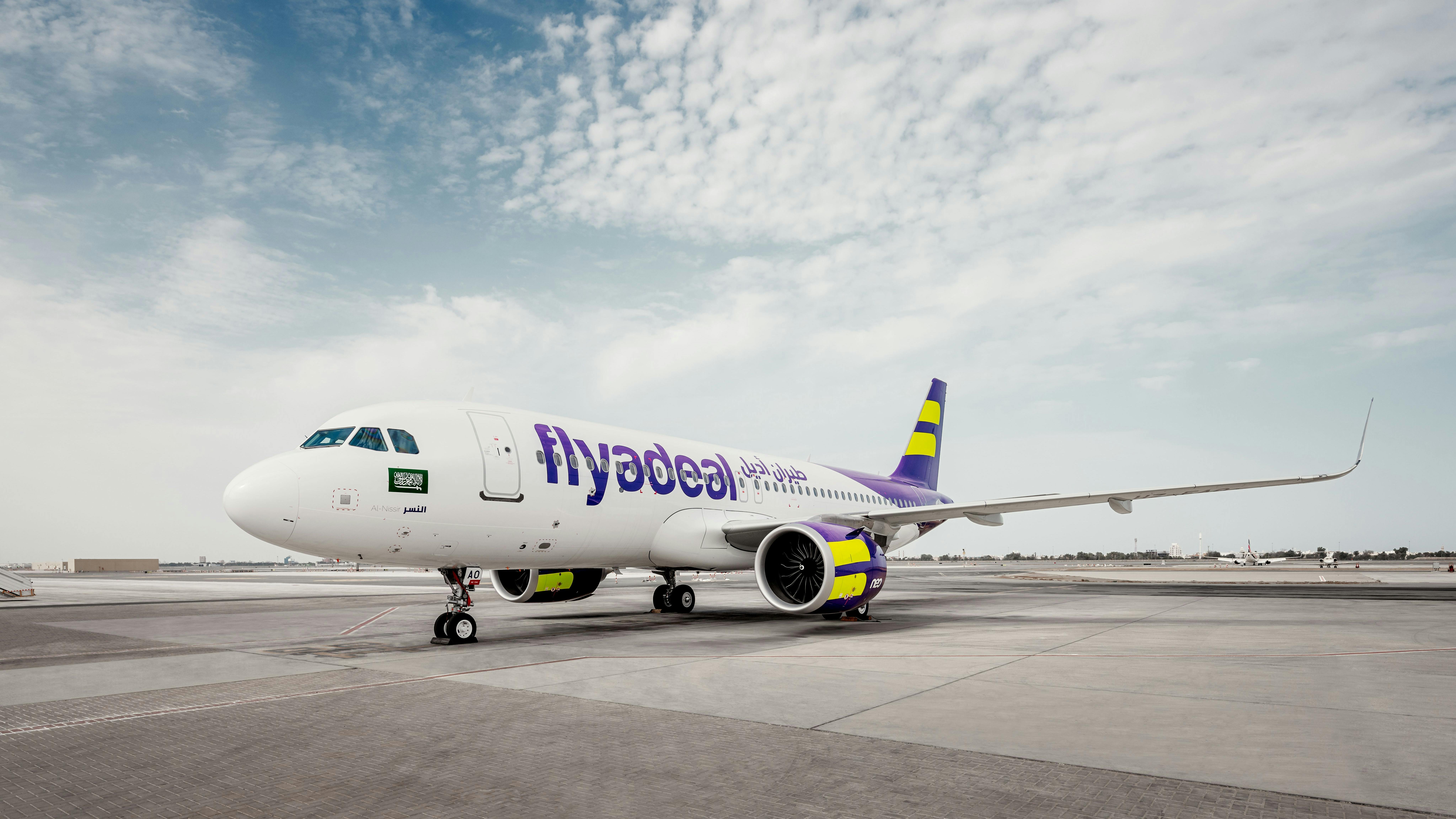 A white airplane with blue and yellow accents and text on the side that reads: flyadeal