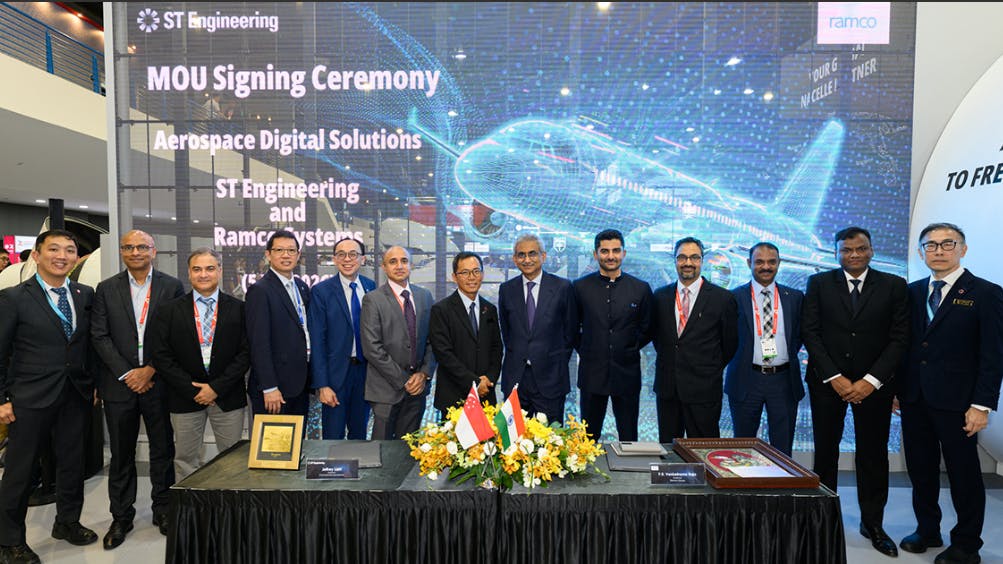 A group of professionals wearing suits standing behind a table and smiling in front of a backdrop that reads: ST Engineering MOU Signing Ceremony Aerospace Digital Solutions