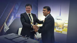 Two men wearing suits shaking hands while standing in front of a projection of an airplane, with a table in front of them holding two pieces of paper and a pen Two men wearing suits shaking hands while standing in front of a projection of an airplane, with a table in front of them holding two pieces of paper and a pen
