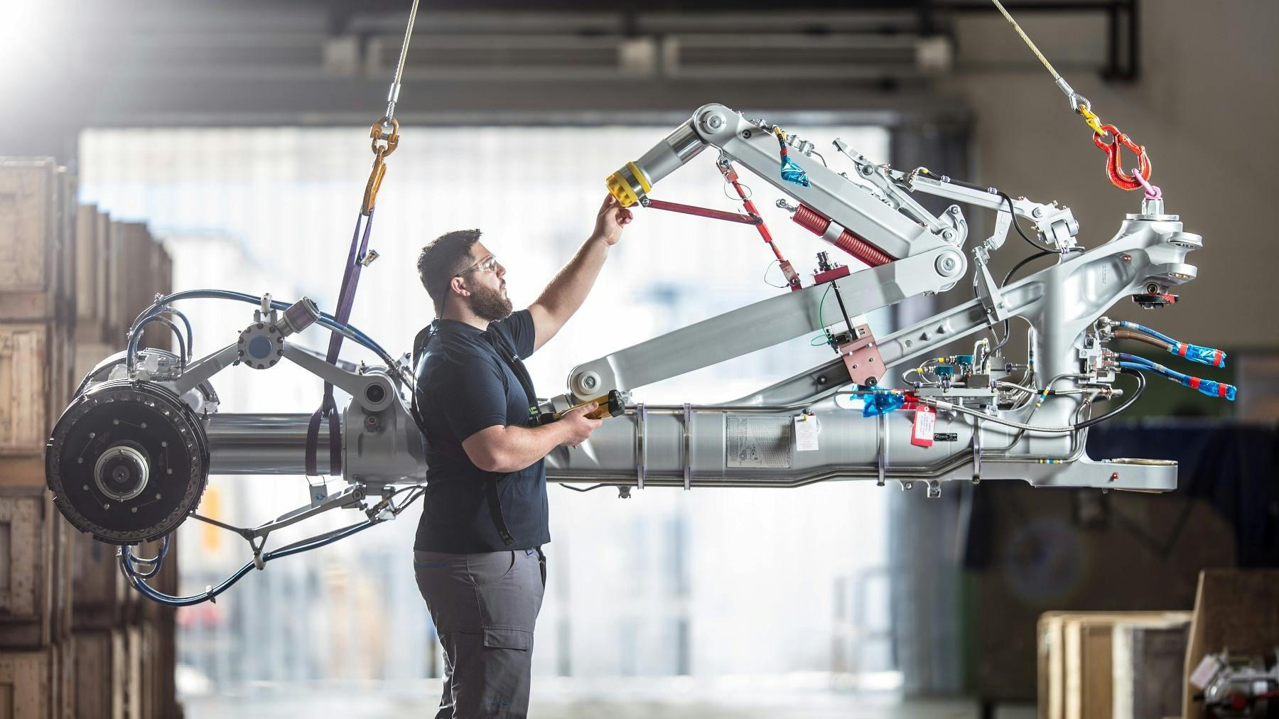 A technician working on a piece of airplane landing gear that's being suspended in the air by cables