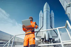 A technician wearing an orange high-visibility suit and hard hat holding a tablet while standing in front of a space shuttle preparing for launch A technician wearing an orange high-visibility suit and hard hat holding a tablet while standing in front of a space shuttle preparing for launch
