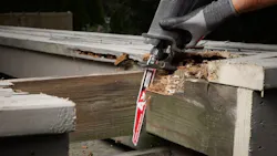 A pair of hands wearing black gloves using a red and white saw blade to cut through a piece of wood A pair of hands wearing black gloves using a red and white saw blade to cut through a piece of wood