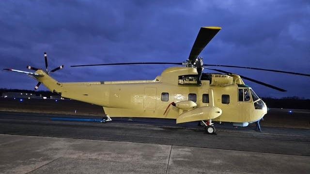 A beige helicopter parked on a tarmac in dim evening lighting