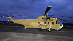 A beige helicopter parked on a tarmac in dim evening lighting A beige helicopter parked on a tarmac in dim evening lighting