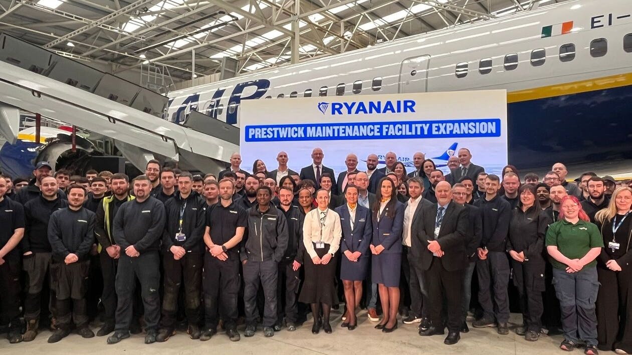 A huge crowd of professionals in business attire standing in a hangar in front of a parked airplane and a sign that reads: RYANAIR Prestwick Maintenance Facility Expansion