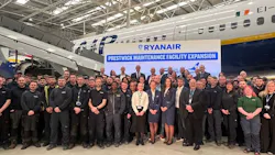 A huge crowd of professionals in business attire standing in a hangar in front of a parked airplane and a sign that reads: RYANAIR Prestwick Maintenance Facility Expansion A huge crowd of professionals in business attire standing in a hangar in front of a parked airplane and a sign that reads: RYANAIR Prestwick Maintenance Facility Expansion