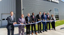 A line of professionals wearing business attire smiling at the camera while standing by a large ribbon during a ribbon-cutting ceremony A line of professionals wearing business attire smiling at the camera while standing by a large ribbon during a ribbon-cutting ceremony