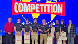 A group of young adults holding gift bags with one holding a trophy, standing in a line between older professionals, under a banner that reads: COMPETITION A group of young adults holding gift bags with one holding a trophy, standing in a line between older professionals, under a banner that reads: COMPETITION
