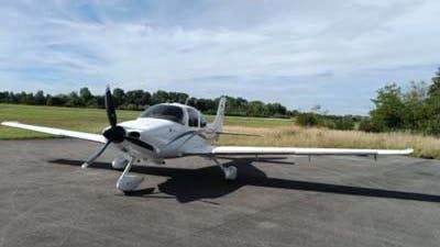A small white airplane parked on a tarmac outside next to a field of grass