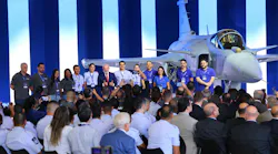 A line of people wearing blue polo shirts standing on stage in front of an airplane in front of a large crowd A line of people wearing blue polo shirts standing on stage in front of an airplane in front of a large crowd