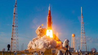 A rocket launching from a station on the ground with flames coming out from the bottom and plumes of smoke