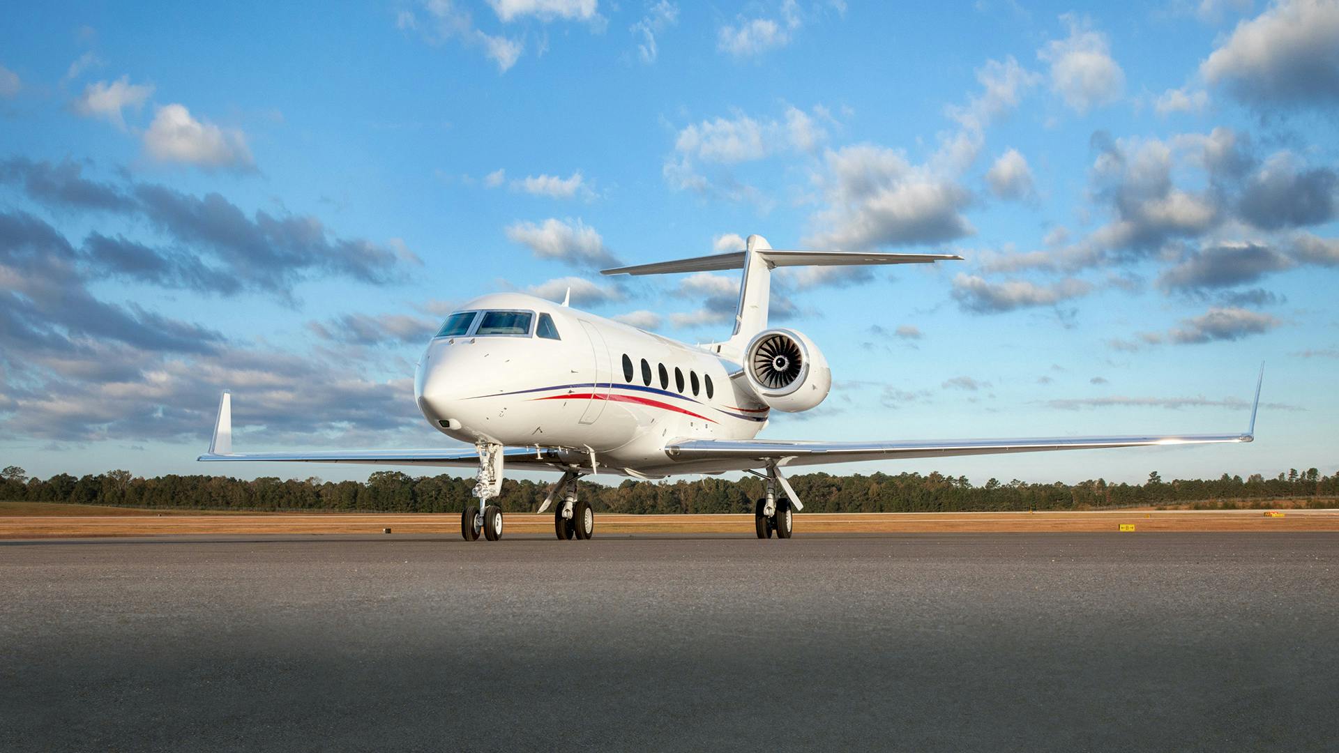 A white airplane with red and green stripes on the side parked on a tarmac outdoors with a blue sky behind it