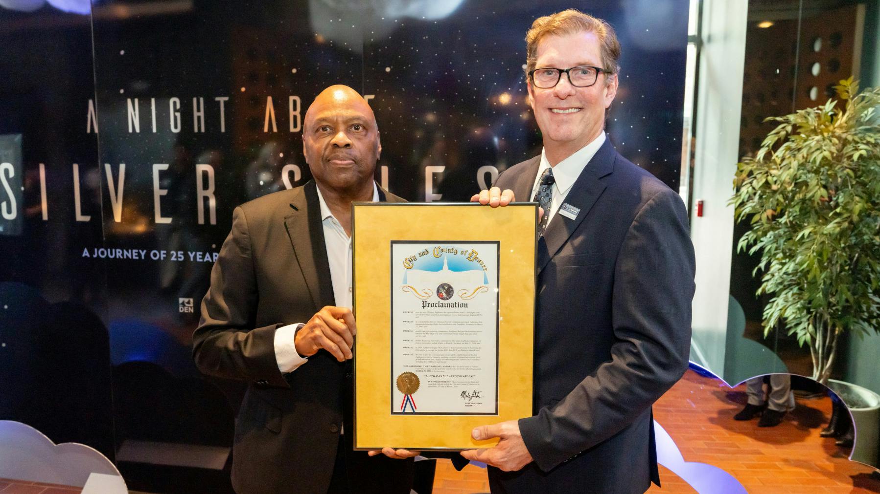 Phil Washington, DEN CEO and Don Bunkenburg, Lufthansa Group Senior Director Sales Western USA, CENAM and Global Accounts, with Denver Mayor Mike Johnston's official proclamation.