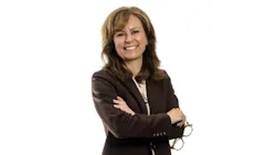 A woman wearing a brown suit and holding a pair of eyeglasses smiling at the camera A woman wearing a brown suit and holding a pair of eyeglasses smiling at the camera