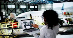 A woman in an aircraft hangar looking at an airplane in the distance and holding a laptop showing a rendering of an engine A woman in an aircraft hangar looking at an airplane in the distance and holding a laptop showing a rendering of an engine