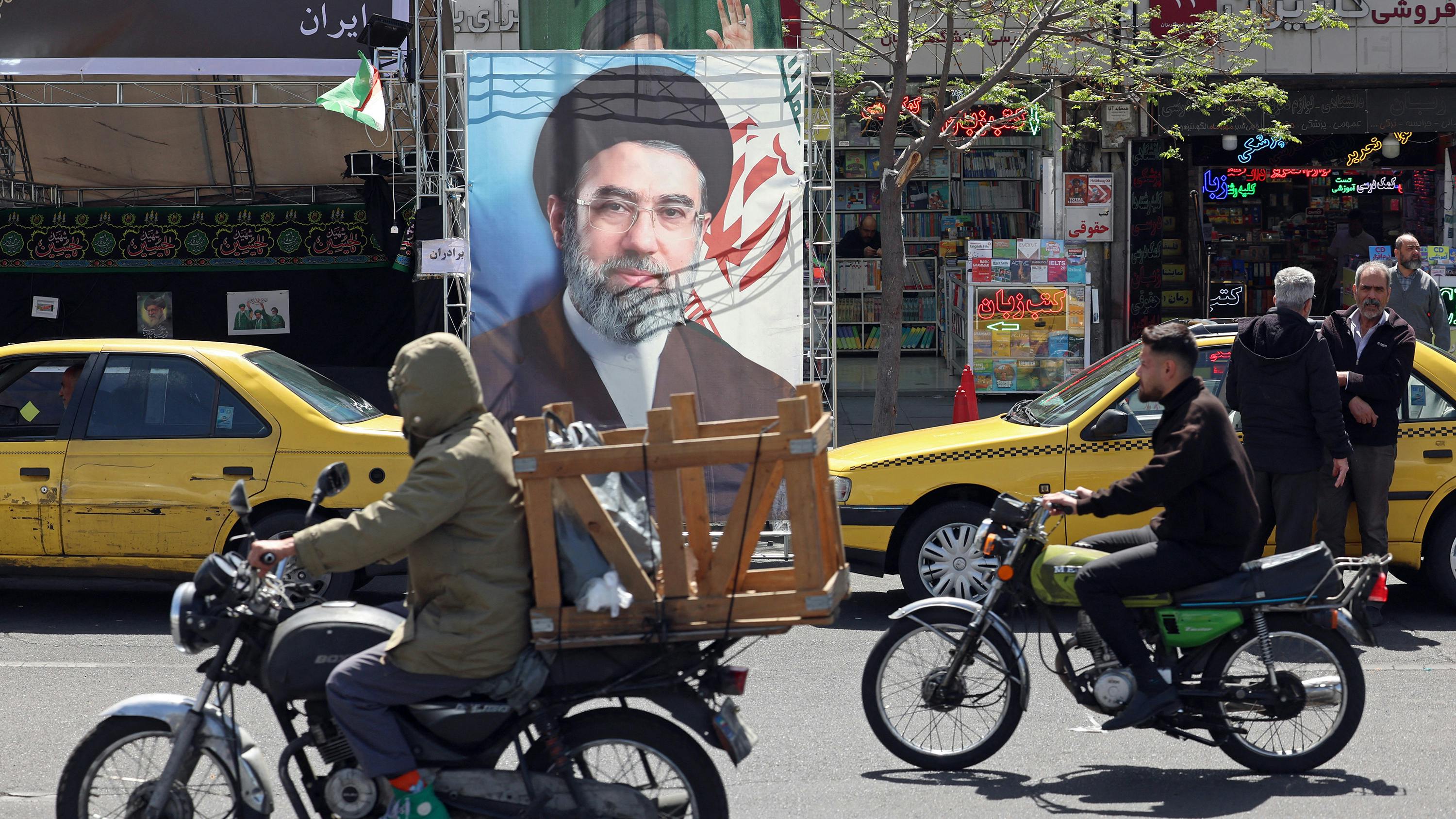 Two people riding bikes in the street of a city with businesses behind them