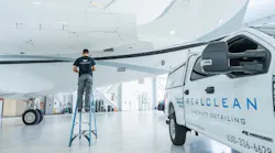 A man standing on a ladder near an airplane with a van parked next to him that has text on the side reading: RealClean Aircraft Detailing A man standing on a ladder near an airplane with a van parked next to him that has text on the side reading: RealClean Aircraft Detailing