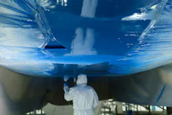 A person wearing a white PPE suit and blue gloves underneath an airplane that's all painted blue A person wearing a white PPE suit and blue gloves underneath an airplane that's all painted blue