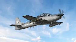 A dark gray military aircraft flying in a blue sky, with the words 'A-29 Super Tucano' printed on the side A dark gray military aircraft flying in a blue sky, with the words 'A-29 Super Tucano' printed on the side