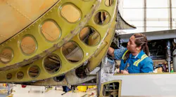 A woman wearing a blue shirt and high-visibility vest working on an airplane that's showing signs of rust A woman wearing a blue shirt and high-visibility vest working on an airplane that's showing signs of rust