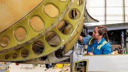 A woman wearing a blue shirt and high-visibility vest working on an airplane that's showing signs of rust A woman wearing a blue shirt and high-visibility vest working on an airplane that's showing signs of rust