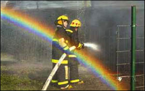 Firefighters use a hose line on a burning barn full of farm equipment and hay on the Bertels farm Monday morning as sunlight, refracting through spray from another fire hose, creates a rainbow behind the firefighters.