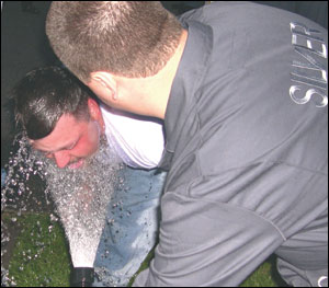 An OC pepper spray victim is rinsed with cool water from a garden hose. He will then be directed to dry himself with a clean cloth and report to paramedics for an evaluation.