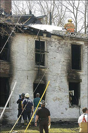 A firefighter sprays water on the roof of a house where a fire killed three people and injured two others near the campus of Miami University, Sunday, April 10, 2005, in Oxford, Ohio. (AP Photo/David Kohl)
