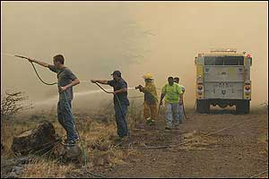Residents armed with garden hoses assist a firefighter along a dirt maintenance road as fire threatens the Waikoloa Village housing subdivision on the Big Island of Hawaii, Tuesday, Aug 2, 2005. The dirt road served as a fire break and kept the fire from burning several nearby houses.