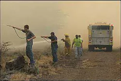 Residents armed with garden hoses assist a firefighter along a dirt maintenance road as fire threatens the Waikoloa Village housing subdivision on the Big Island of Hawaii, Tuesday, Aug 2, 2005. The dirt road served as a fire break and kept the fire from burning several nearby houses. Residents armed with garden hoses assist a firefighter along a dirt maintenance road as fire threatens the Waikoloa Village housing subdivision on the Big Island of Hawaii, Tuesday, Aug 2, 2005. The dirt road served as a fire break and kept the fire from burning several nearby houses.