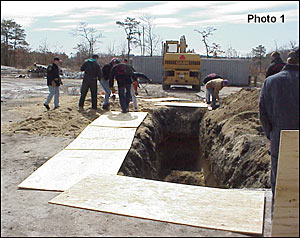 Crews place ground pads around the trench and remove loose soil to the spoil pile on the right.