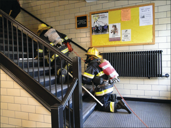 Rapid intervention team members, with masks obscured to simulate smoke conditions, begin the simulated search and lost firefighter.