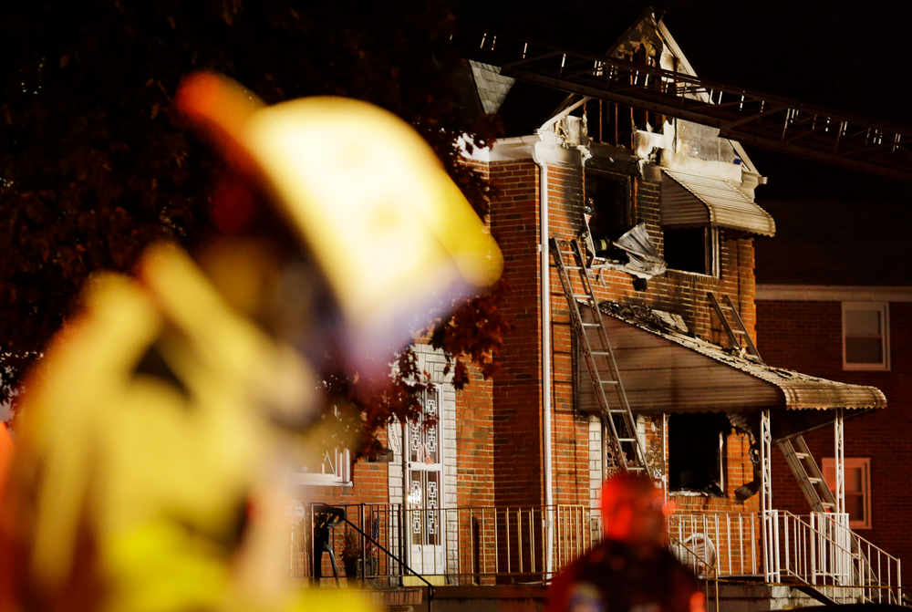 Officials stand in front of a fire-damaged house in Baltimore, where an early morning fire claimed the lives of an adult and four children on Oct. 11.