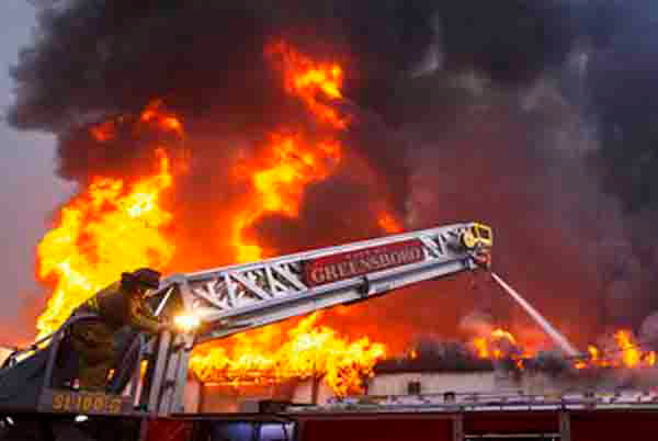Station 7 firefighter Phil Ruff ducks behind the ladder to shield himself from the intense heat as he works the ladder truck nozzle as firefighters battle a two-alarm blaze at Southeast Church Furniture's warehouse at 808 N. Raleigh St. on Friday, January 11, 2013, in Greensboro, N.C.