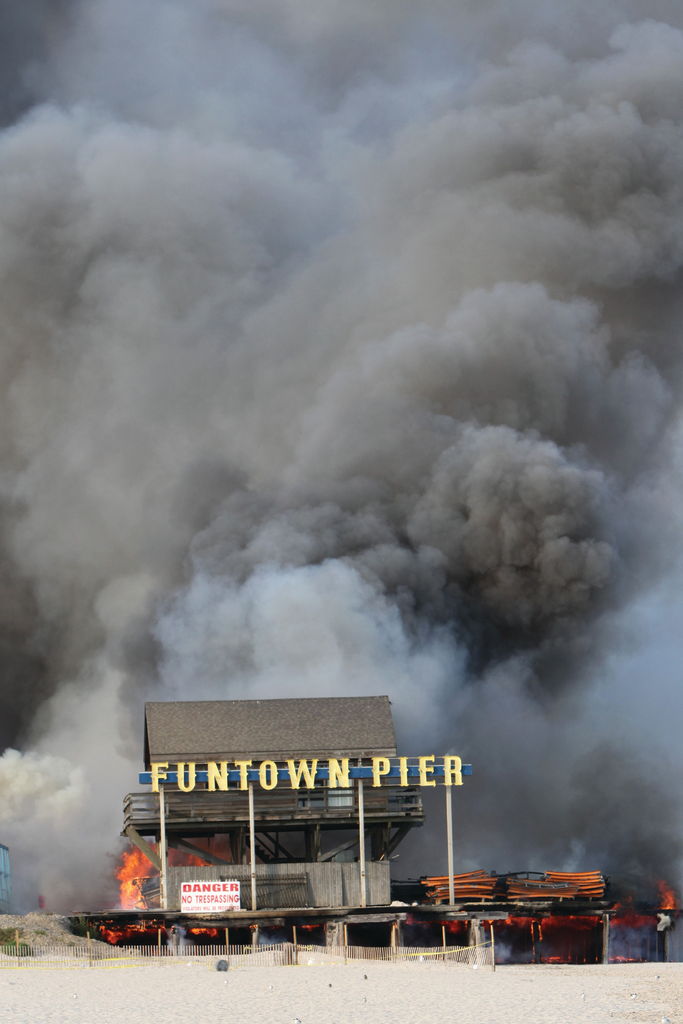 Tremendous rolling smoke is indicative of the wind-swept fire pushing the fire north above and below the boardwalk. The fire extends to the underside of the pier toward the east and the Atlantic Ocean.